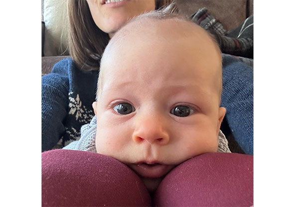 Baby Luca Matthewson is in mom's lap and resting their chin on mom's knees