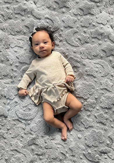 Baby Heidi Canela is laying on a big blanket at home. She is thriving after her Omphalocele surgery and NICU stay